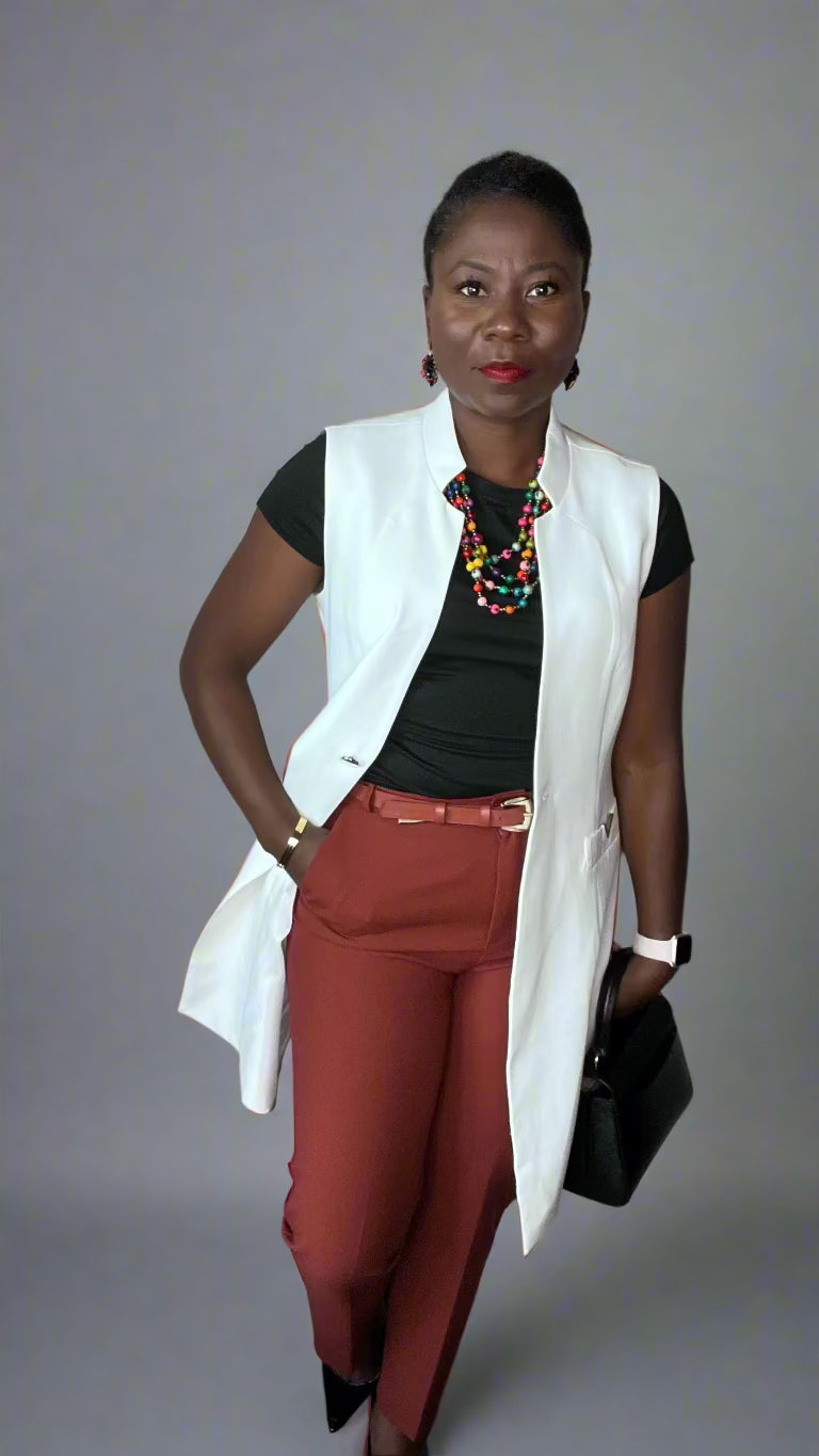 Woman wearing a white vest, black top, red pants, and holding a black clutch against a plain wall.