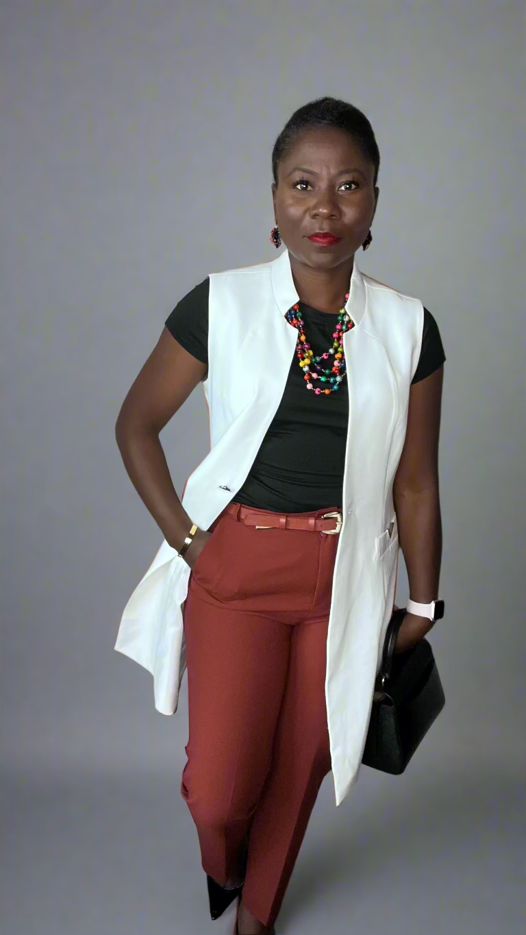 Woman wearing a white vest, black top, red pants, and holding a black clutch against a plain wall.